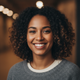 A diverse woman in her late 20s smiling genuinely, with a warm amber and deep charcoal background.